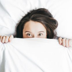 woman hiding half her face under the covers